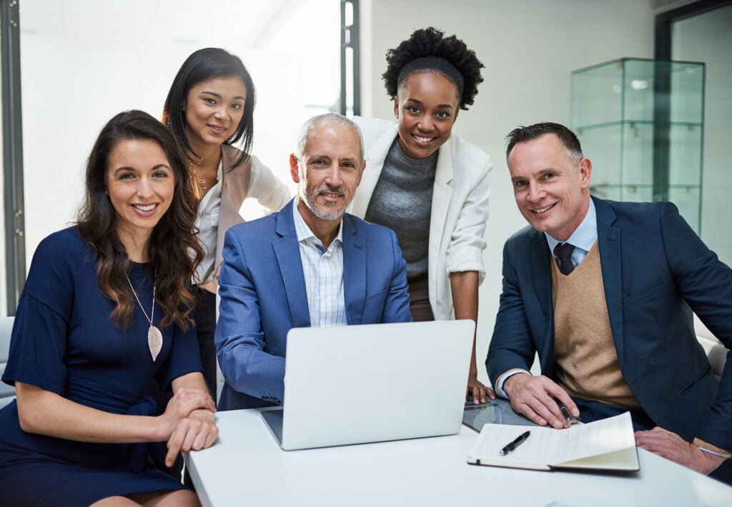 SEO Five colleagues gather around a laptop at a white table in an office, smiling confidently at the camera, their energy reflecting the success of Burnesseo SEO Services.