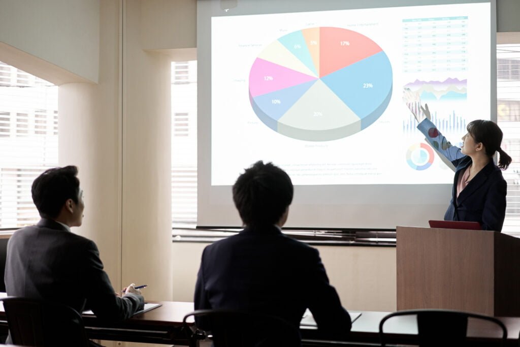 SEO A person presents a pie chart and graphs on a screen to an audience in a conference room, highlighting the impact of Burnesseo SEO Services on digital growth.