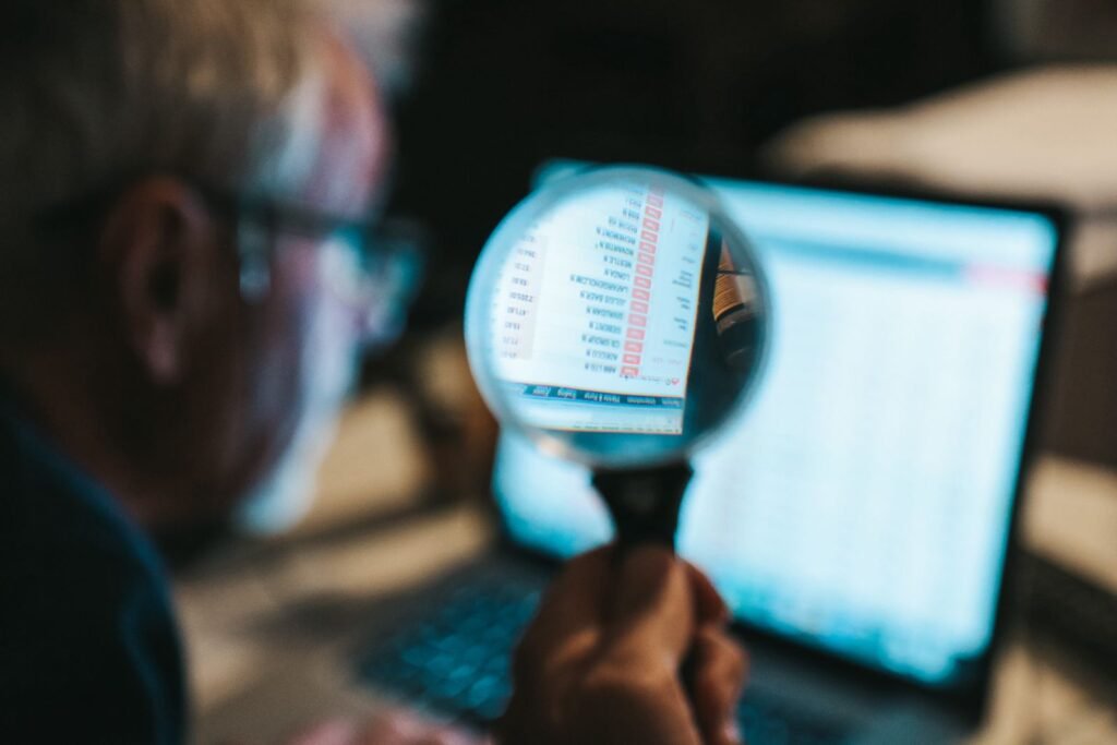 SEO A person holds a magnifying glass close to a computer screen, with text and numbers visible through the glass.